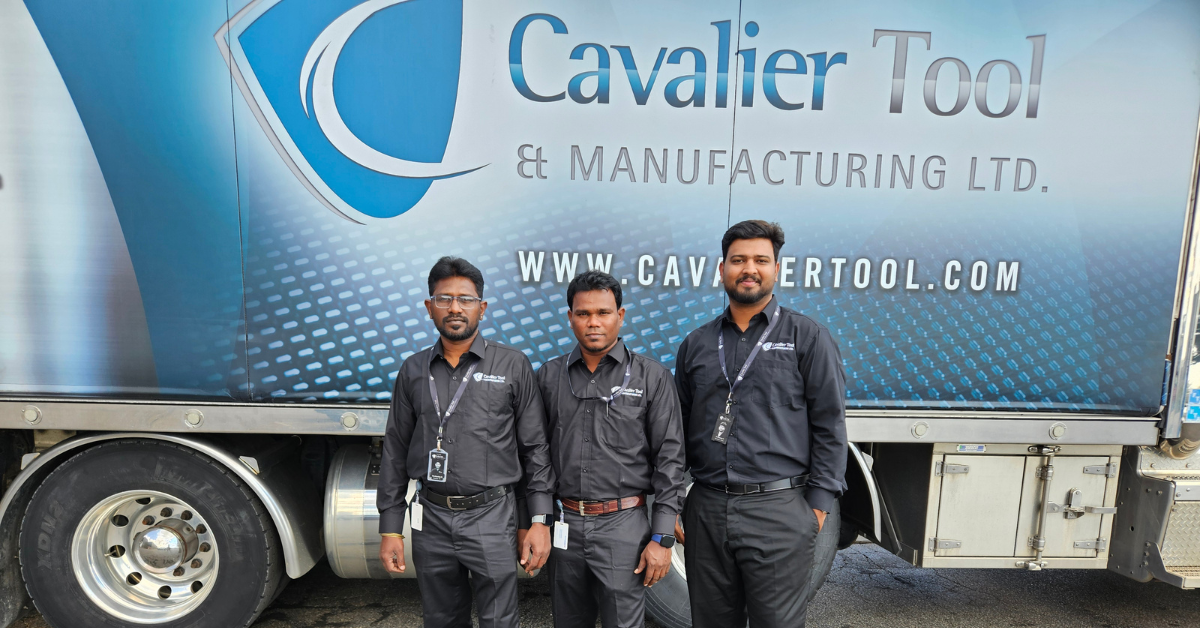 The three team member from India (left to right: Vella, Mani, Nandha) stand in front of one of Cavalier's large Peterbilt Trucks. This particular truck is used to ship molds across internationally. The main destinations for this truck are across the United States. The truck is blue and the Cavalier Logo is featured prominently in the middle. Underneath the logo is cavalier's website URL, WWW.CAVALIERTOOL.COM.